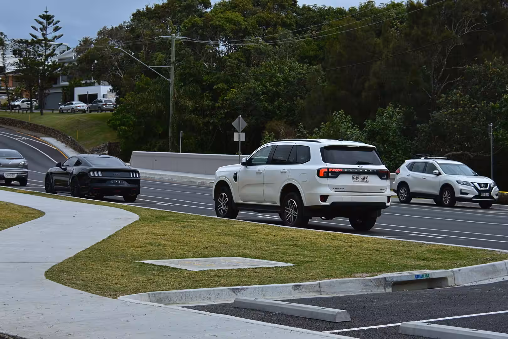 A white Ford Everest drives along a tree-lined road beside a black muscle car.