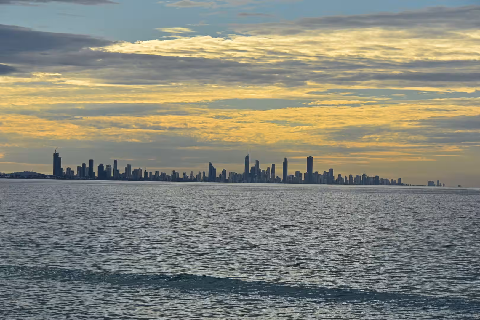 A long city skyline traces the far shore under a glowing band of sunset clouds.