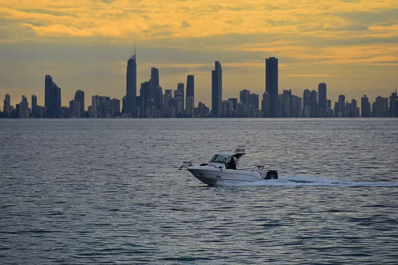 A white motorboat cuts across calm water beneath a golden sky.