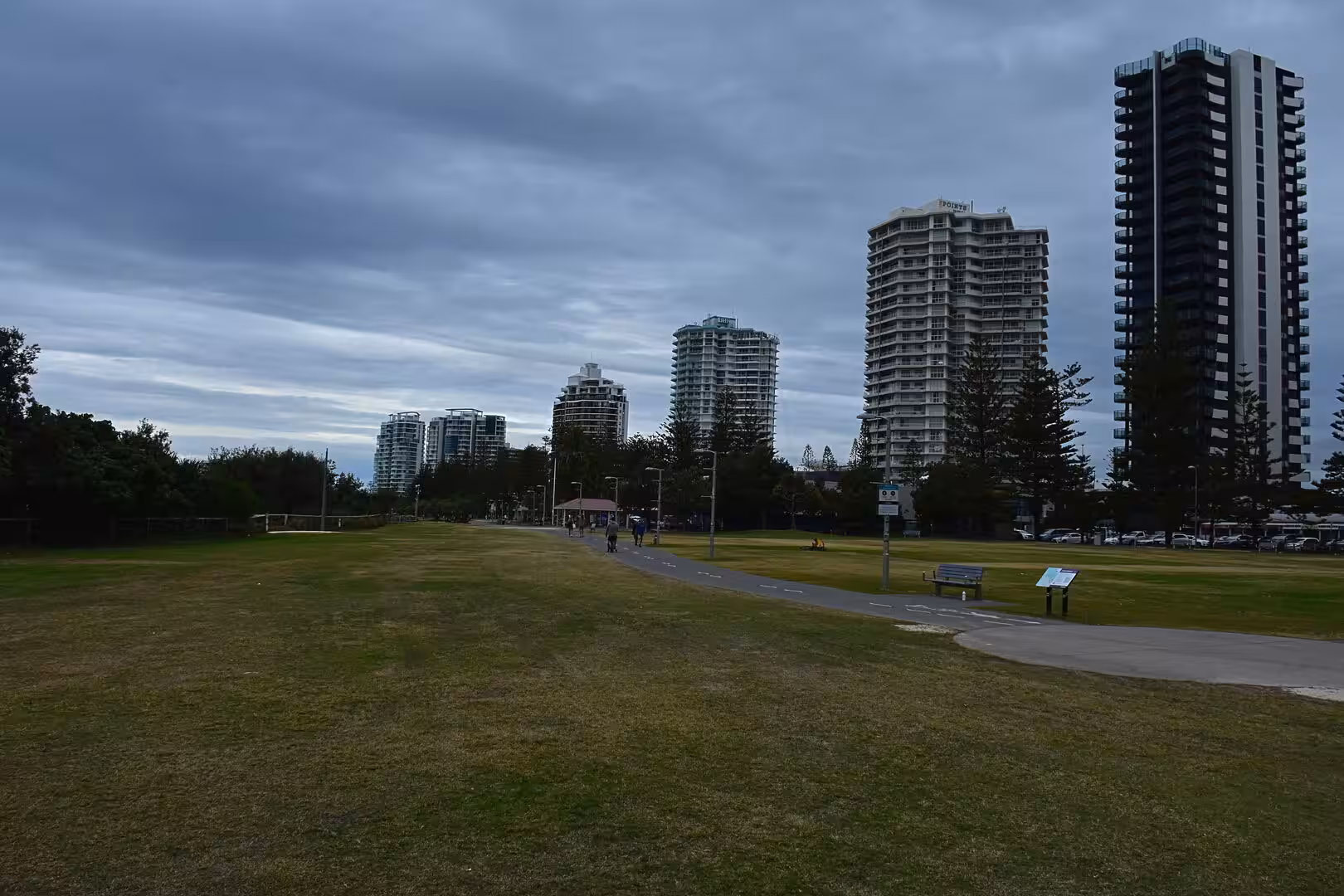 A grassy park path curves beneath towers under a cloudy sky.