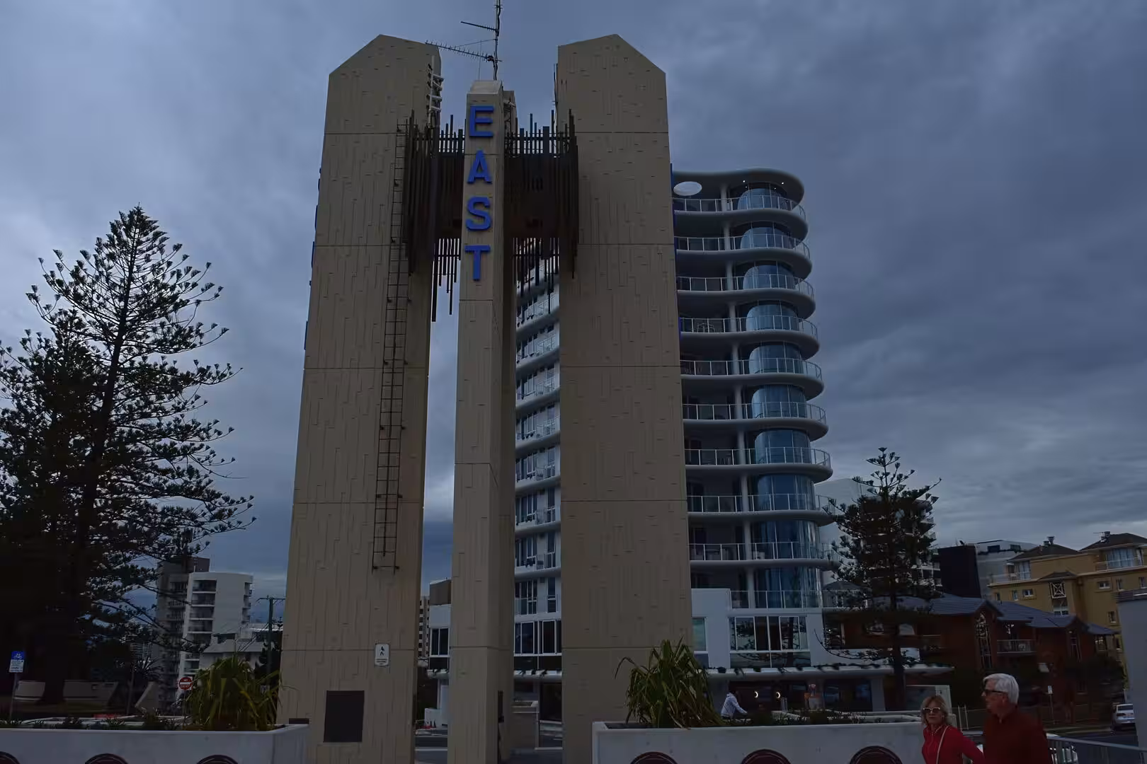Tall concrete pylons topped with a sign spelling EAST stand against a high-rise apartment building.