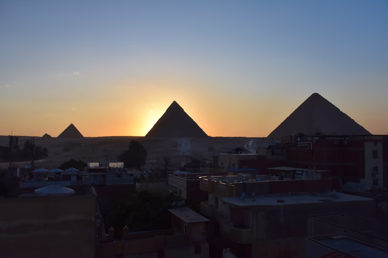Pyramids glow on the horizon as the sun sinks behind their peaks.