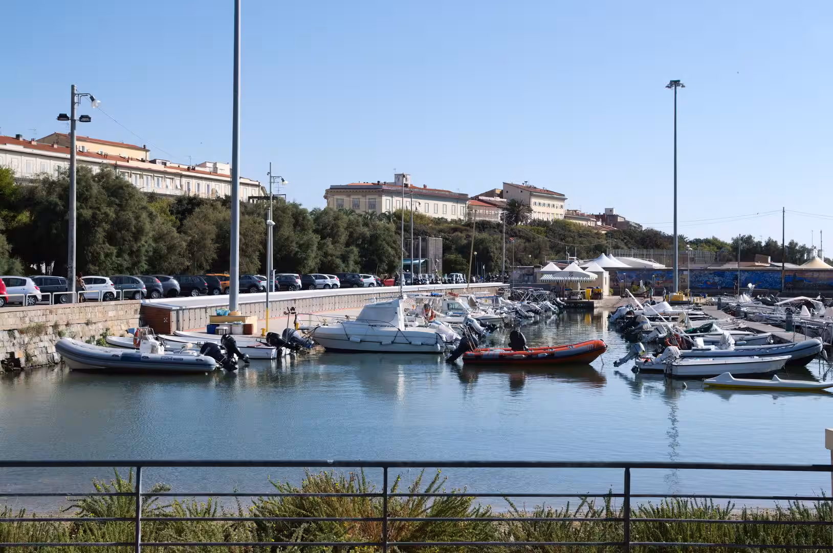 A cluster of boats rests at a stone quay below a hillside town on a clear day.