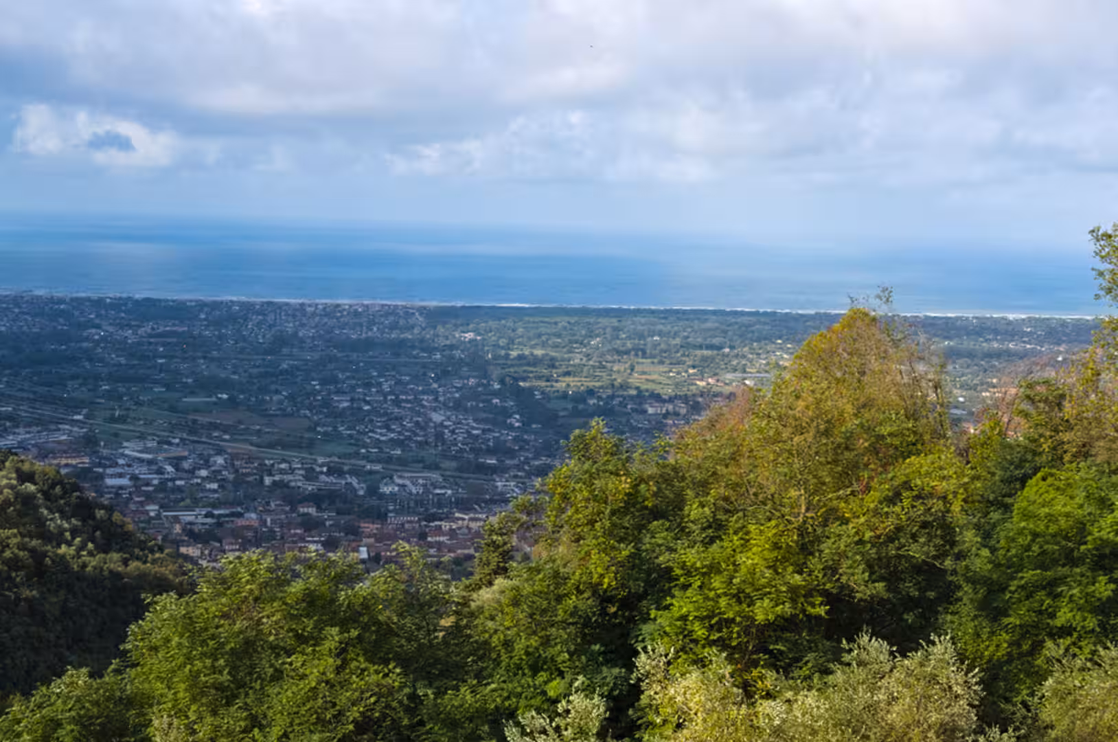 Leafy green hills give way to a sprawling town and a distant blue sea.