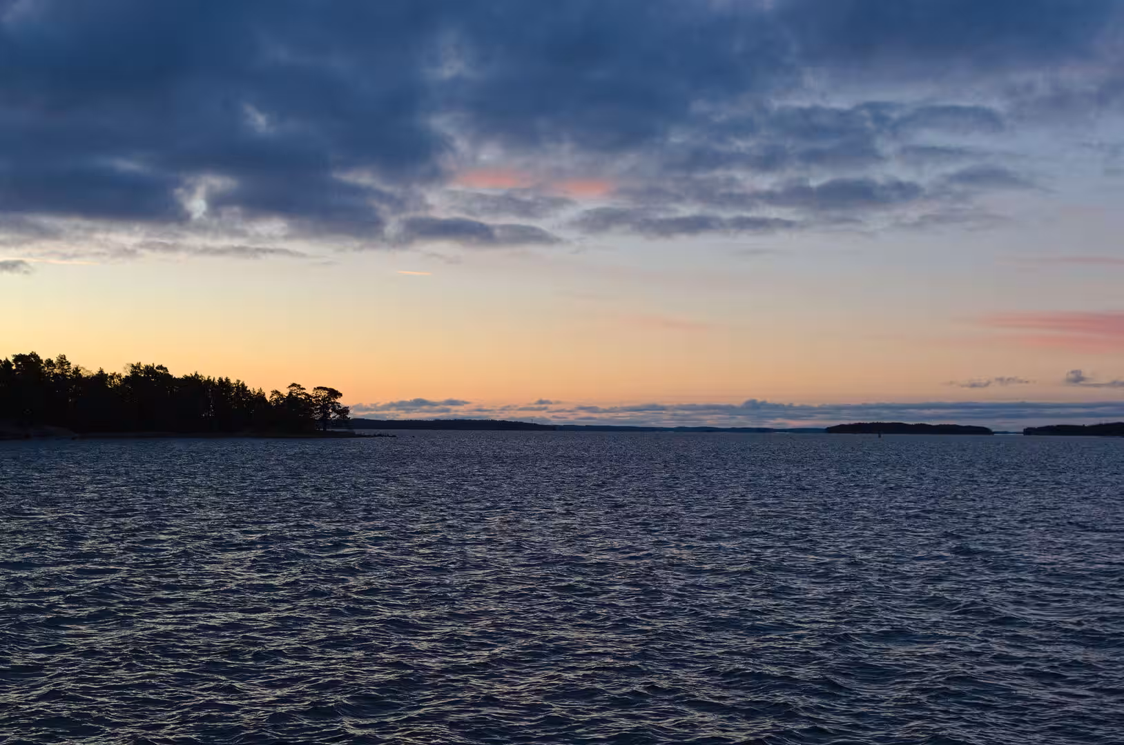 Dark rippling water stretches toward a low orange glow under a heavy evening cloudscape.