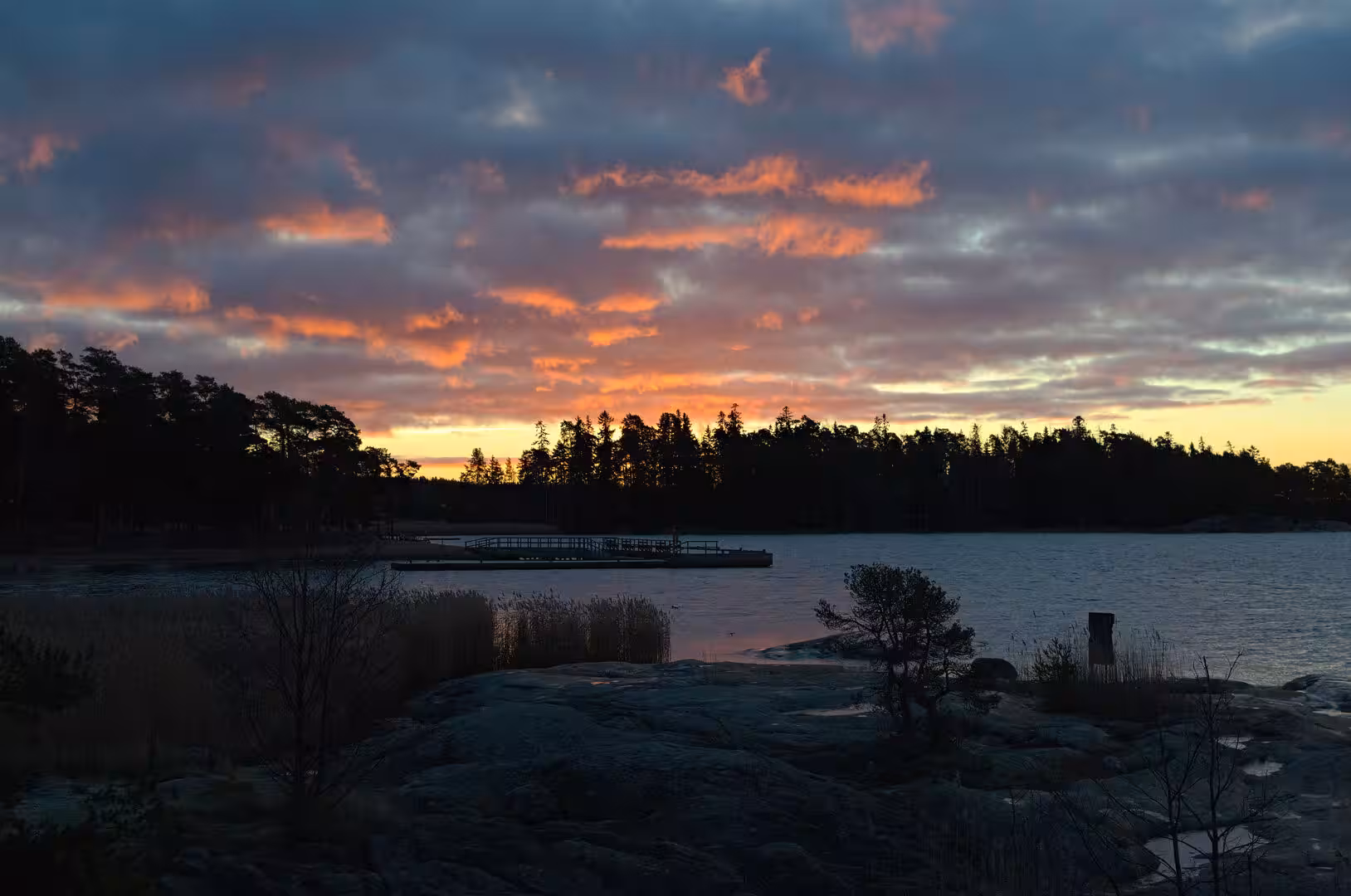 Orange streaks of cloud hang low over black still water.