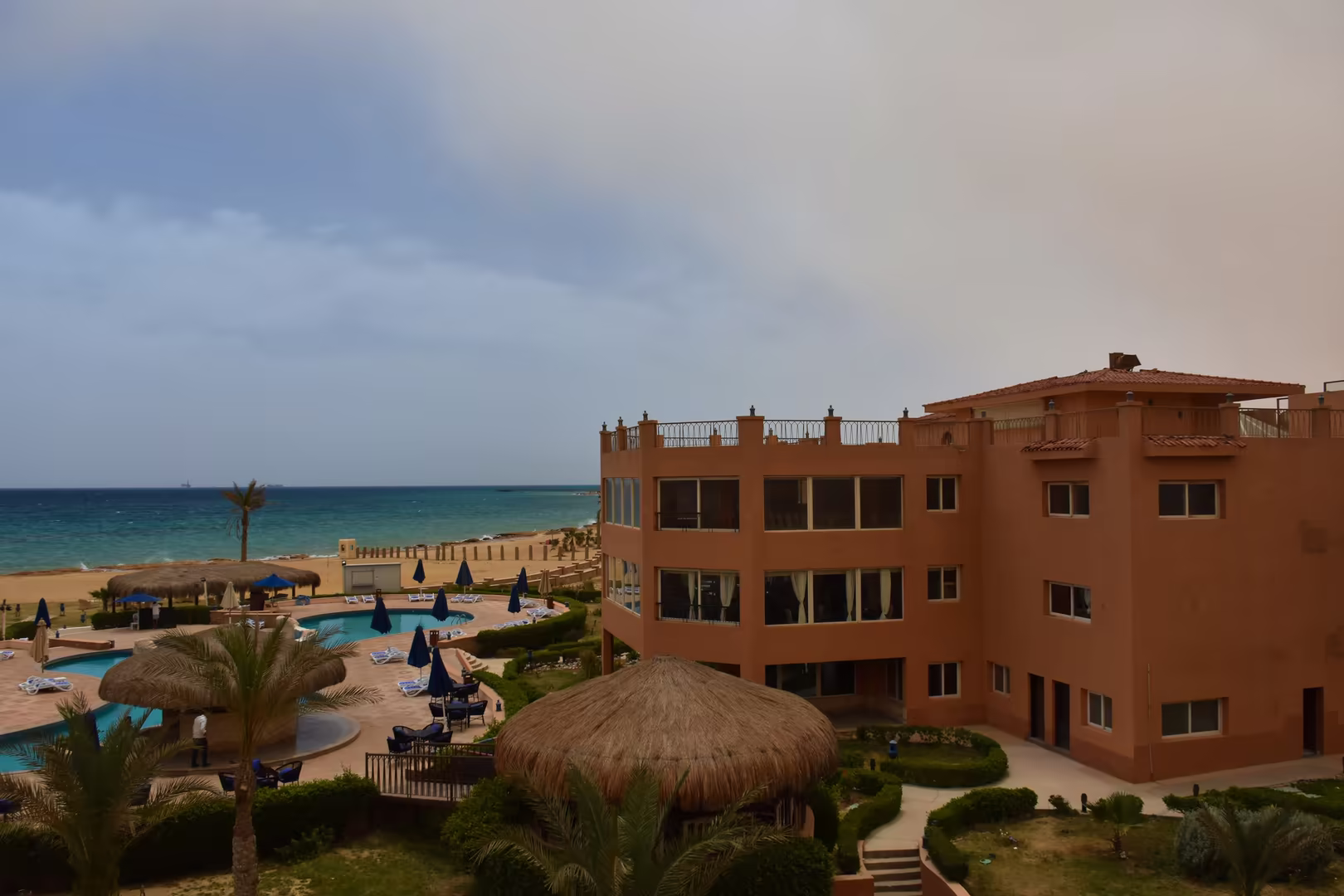 A rustic red hotel towers over palm-fringed pools and a sandy beach.