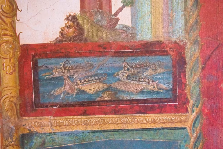 A weathered fresco depicting a naval battle scene framed in red, with a lion head above.