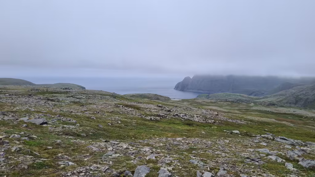 Steep dark cliffs descend to a calm grey sea while low cloud hides the upper slopes of the coastal headland, at the North Cape in Finnmark, Norway.
