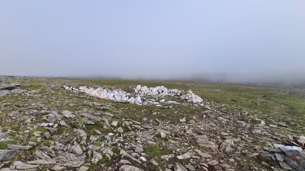 Low grey rocks and patches of grass stretch into dense white mist on open upland ground with no trees in sight, at the North Cape in Finnmark, Norway.
