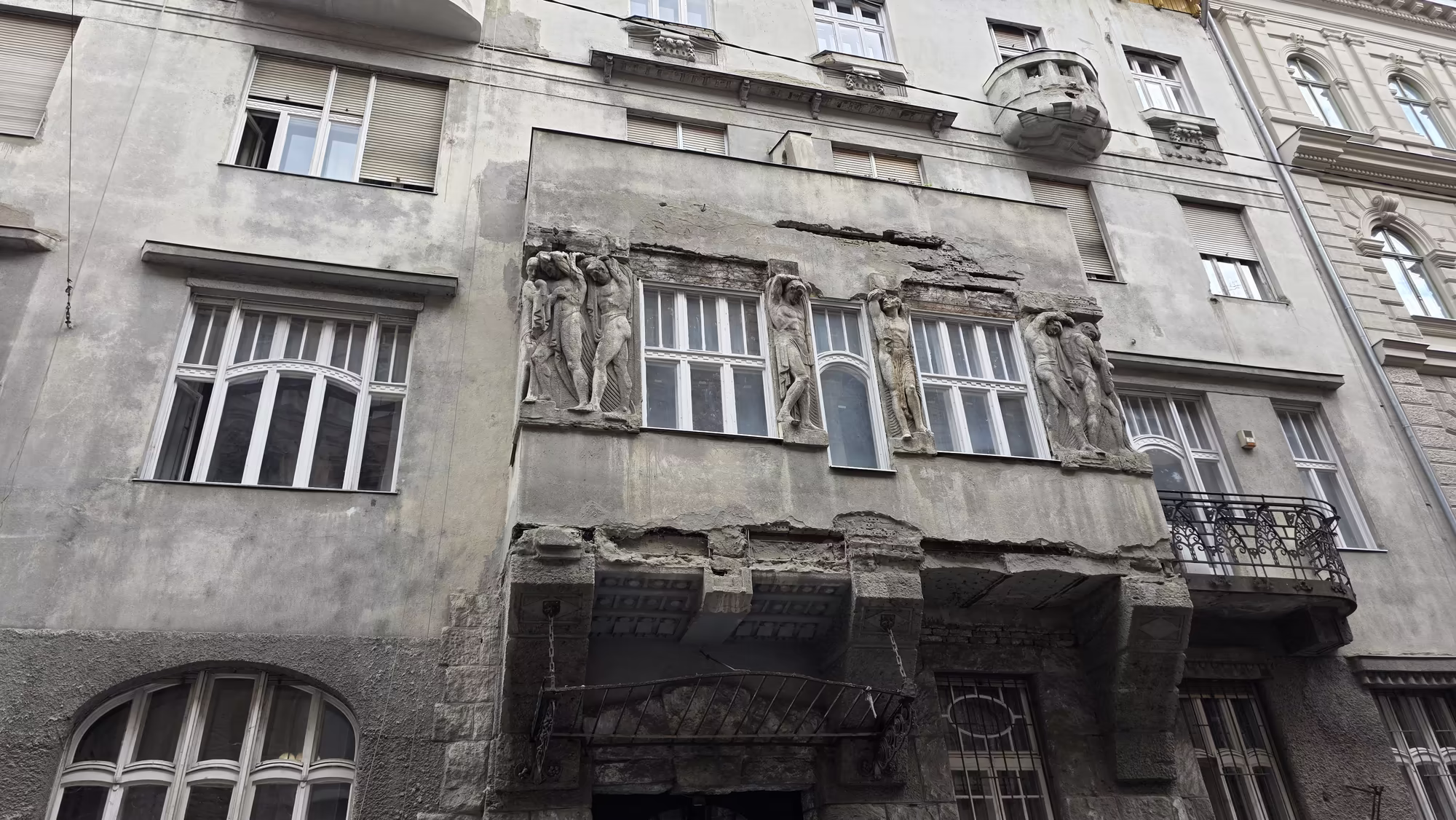 Four sculpted atlantes brace the windows above a heavy stone doorway on the peeling facade of an old eclectic building.